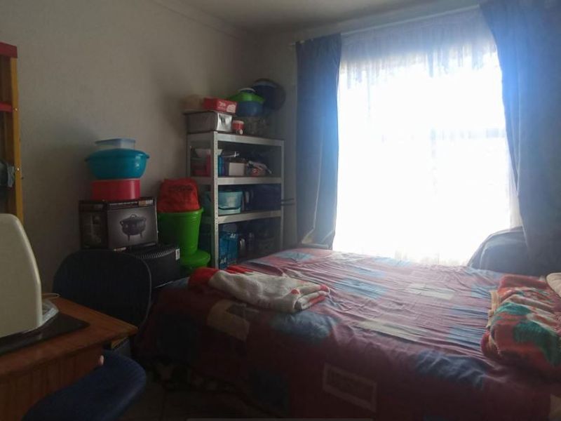 A bedroom featuring a window with curtains, providing natural light. The space is currently used for storage and sleeping.