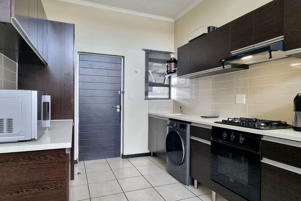 Modern kitchen featuring dark wood cabinetry, light stone countertops, tiled backsplash, built-in oven, gas hob, extractor fan, and integrated laundry plumbing.
