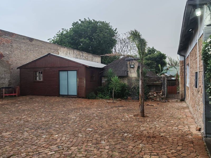 Rear courtyard area featuring cobblestone paving, a timber-clad outbuilding, and a traditional thatched structure, enclosed by a high boundary wall.