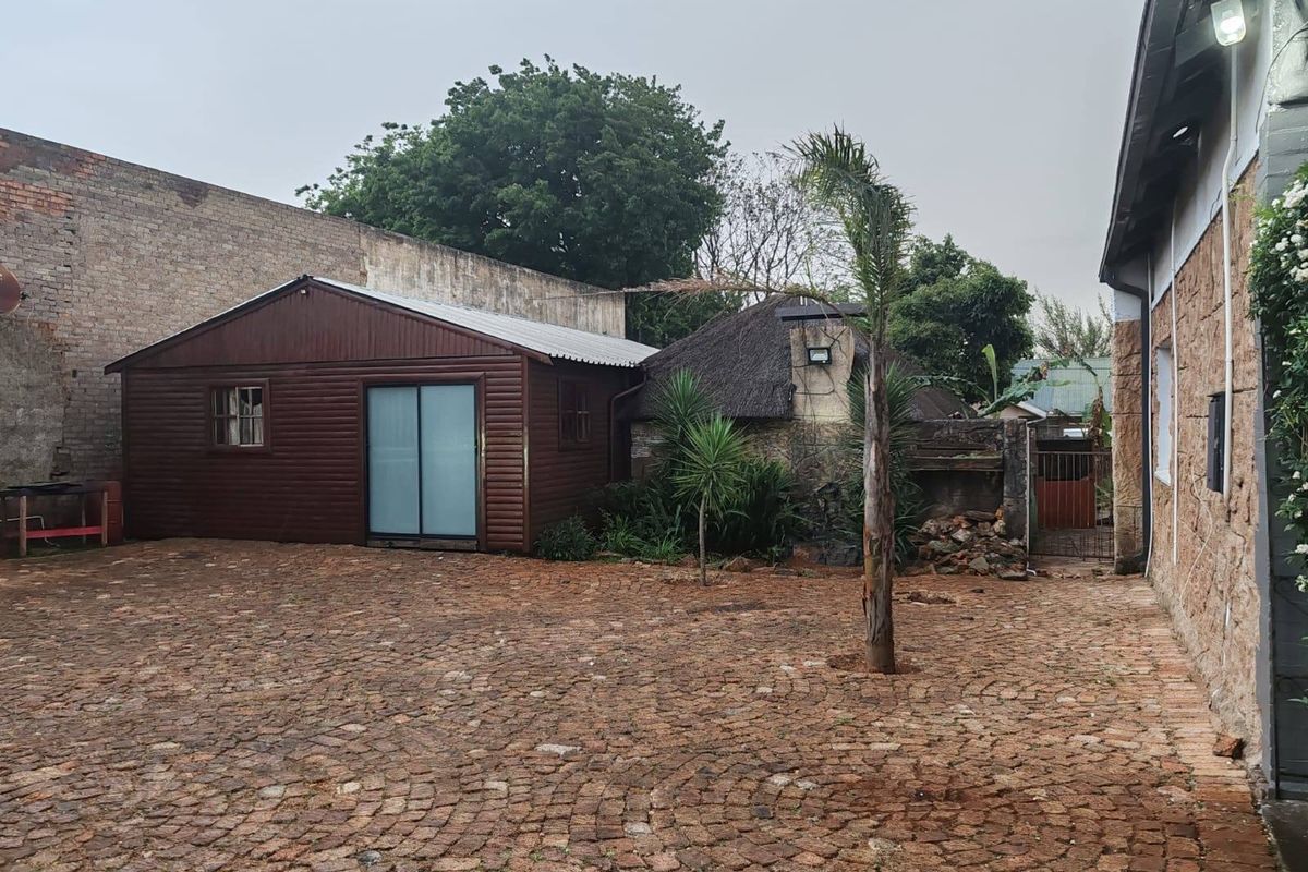 Rear courtyard area featuring cobblestone paving, a timber-clad outbuilding, and a traditional thatched structure, enclosed by a high boundary wall.