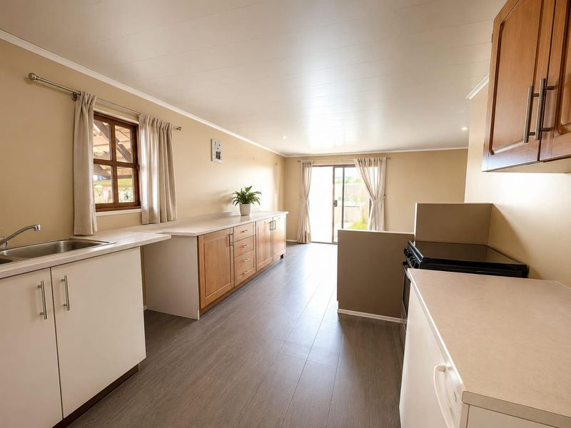 A functional kitchen featuring wood-tone cabinetry, laminate countertops, stainless steel sink, and modern laminate flooring, with direct access to the outdoor area.