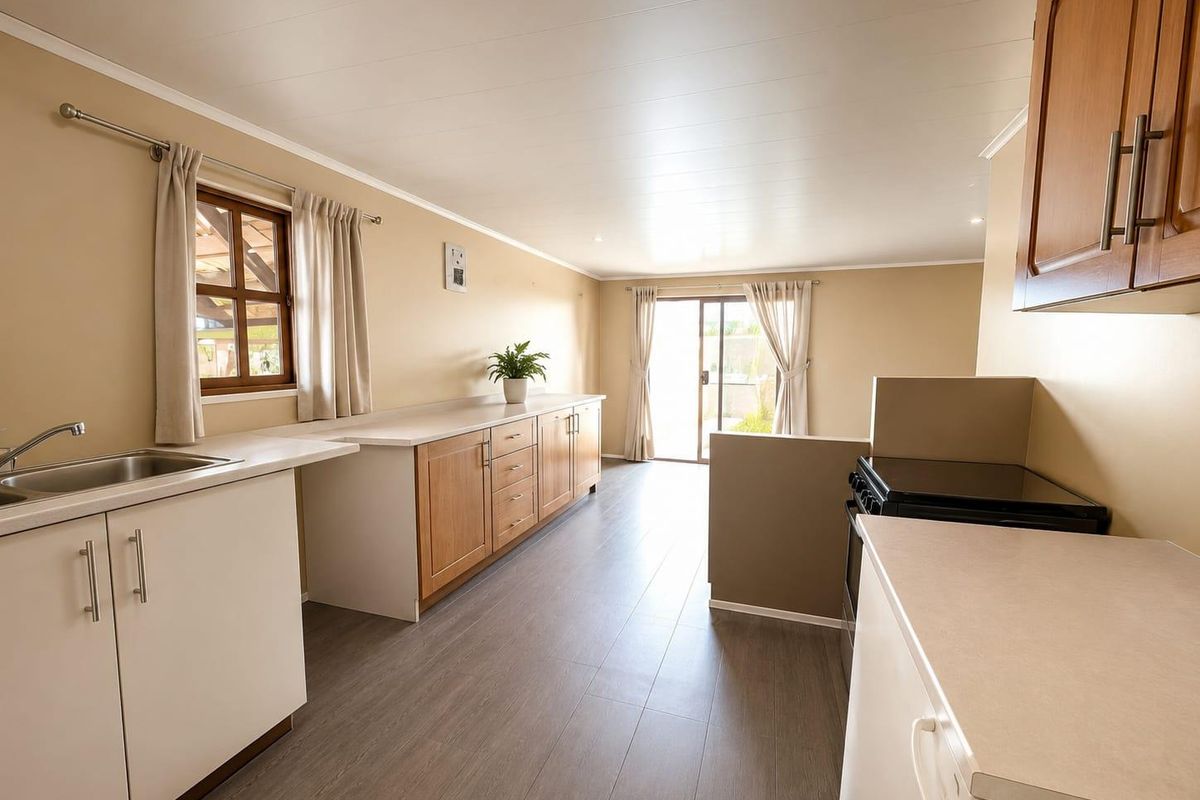 A functional kitchen featuring wood-tone cabinetry, laminate countertops, stainless steel sink, and modern laminate flooring, with direct access to the outdoor area.