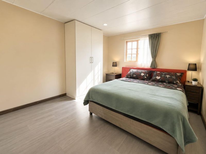 A well-maintained bedroom featuring light-toned laminate flooring, a built-in wardrobe, and a timber-framed window providing natural light.