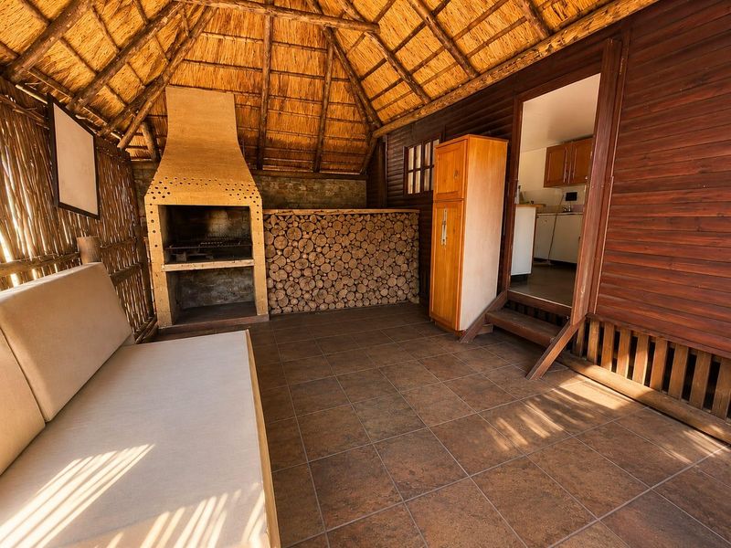 Covered outdoor patio featuring a traditional thatched roof, built-in braai, and tiled flooring, providing a rustic entertainment space with direct access to the kitchen.