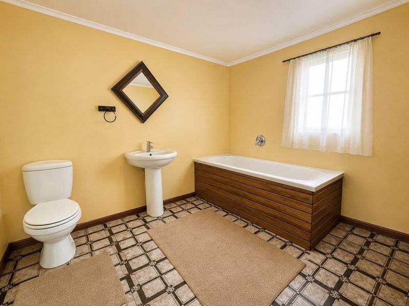 A functional bathroom featuring a pedestal basin, toilet, and a bathtub with a timber-look panel, finished with patterned tiled flooring.