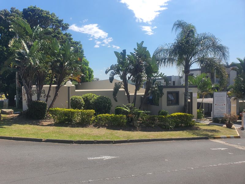 The front entrance and security gatehouse of the apartment complex, featuring established landscaping and a paved approach.