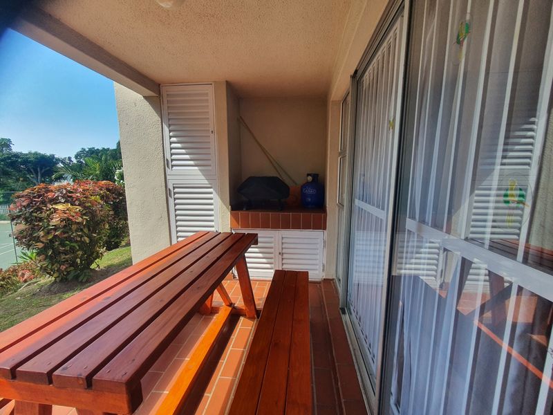 Covered patio area featuring tiled flooring, a built-in braai, and sliding glass door access to the interior living space.