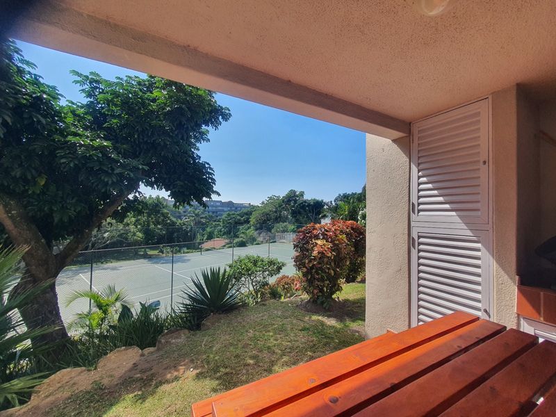 A covered patio area featuring a louvered storage cupboard, overlooking a landscaped garden and tennis court.