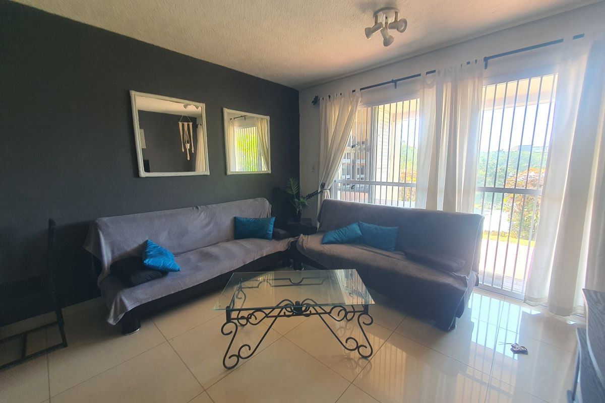 A living room featuring tiled flooring, dark accent wall, and large windows with security bars providing natural light.
