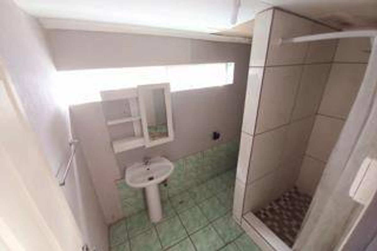 A functional bathroom featuring a pedestal basin, a tiled shower enclosure, and a wall-mounted medicine cabinet with dated tile flooring.
