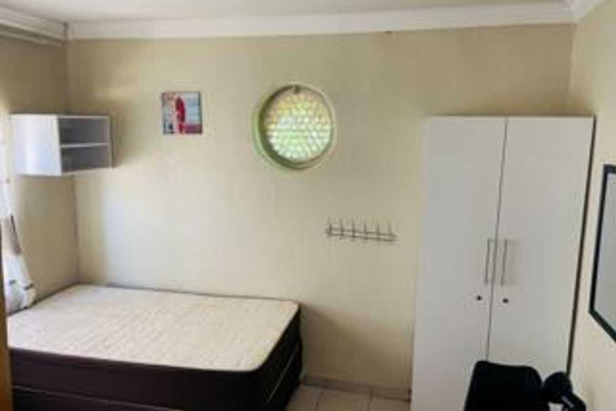 A bedroom featuring a unique porthole window, built-in wardrobe, and wall-mounted shelving, offering a functional space with potential for cosmetic updates.