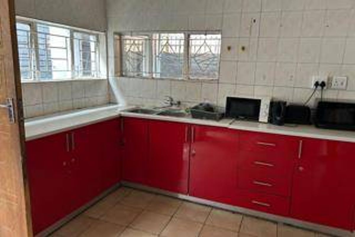 A functional kitchen featuring red cabinetry, tiled backsplash, and double sink, offering a practical layout with potential for modern cosmetic updates.
