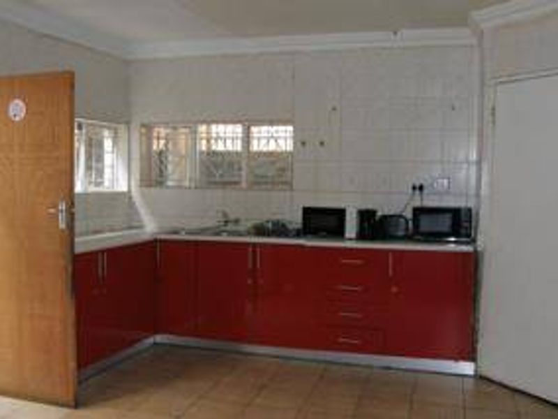 A dated kitchen featuring red cabinetry, tiled backsplash, and tiled flooring, offering a functional layout ready for modern updates.