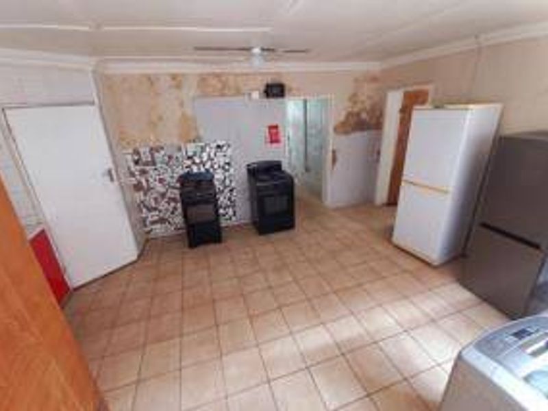 A kitchen area featuring tiled flooring and freestanding stoves, currently requiring significant wall repairs and cosmetic renovation to restore functionality and appeal.