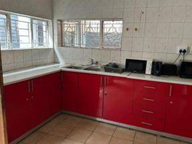 A functional kitchen featuring red cabinetry, tiled backsplash, and double sink, offering a practical layout with potential for modern cosmetic updates.