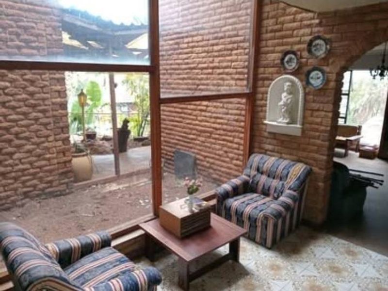 A living area featuring exposed brick walls, large windows overlooking an outdoor space, and tiled flooring, offering a rustic aesthetic with potential for modernization.