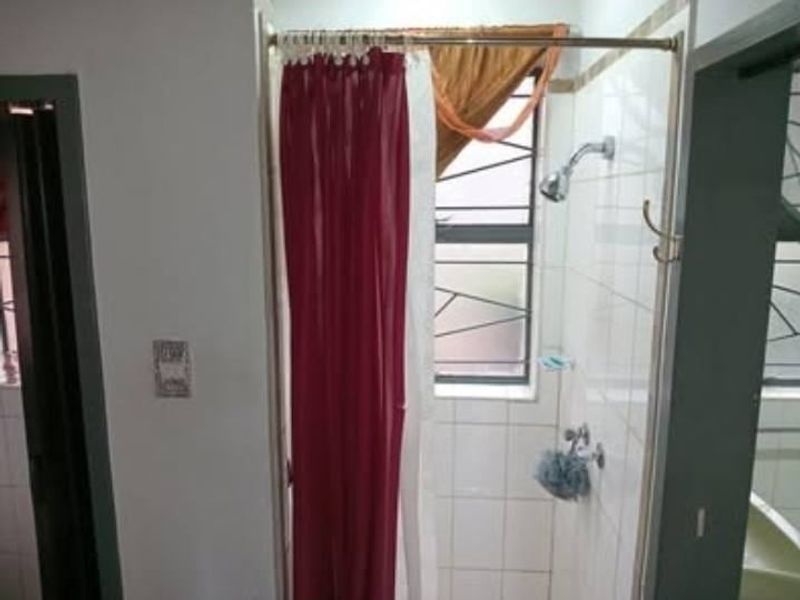 A functional bathroom shower area featuring tiled walls, a shower head, and a window with security bars.