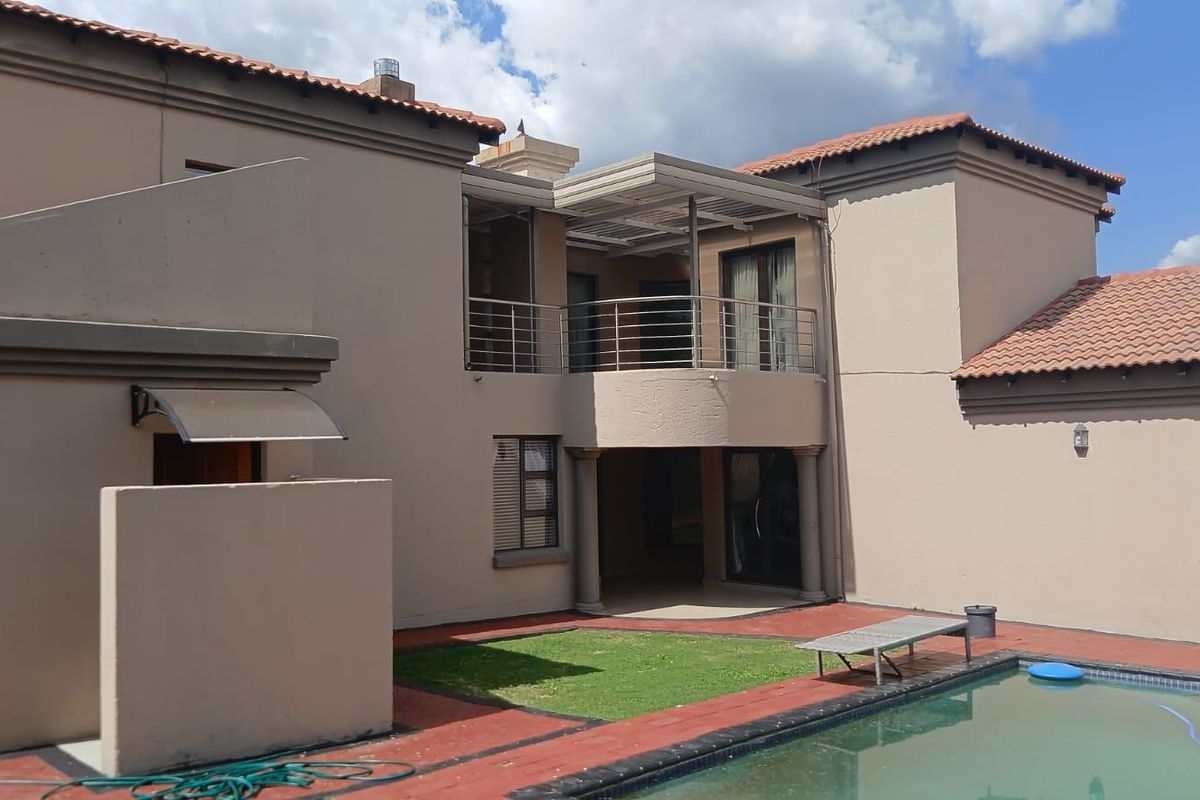 Rear view of the property featuring a swimming pool, paved deck, covered patio, and an upper-level balcony with stainless steel railings.