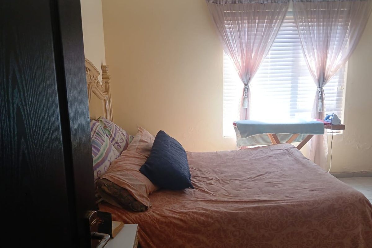 A bedroom featuring tiled flooring and venetian blinds, showing signs of wear on the wall near the window.