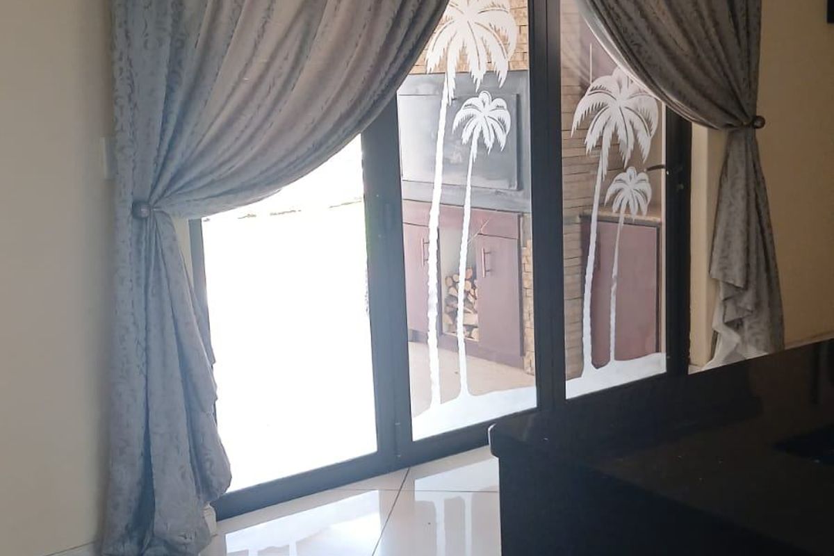 A bright living area featuring polished tile flooring, a decorative crystal chandelier, and sliding glass doors with palm tree etching leading to an outdoor space.