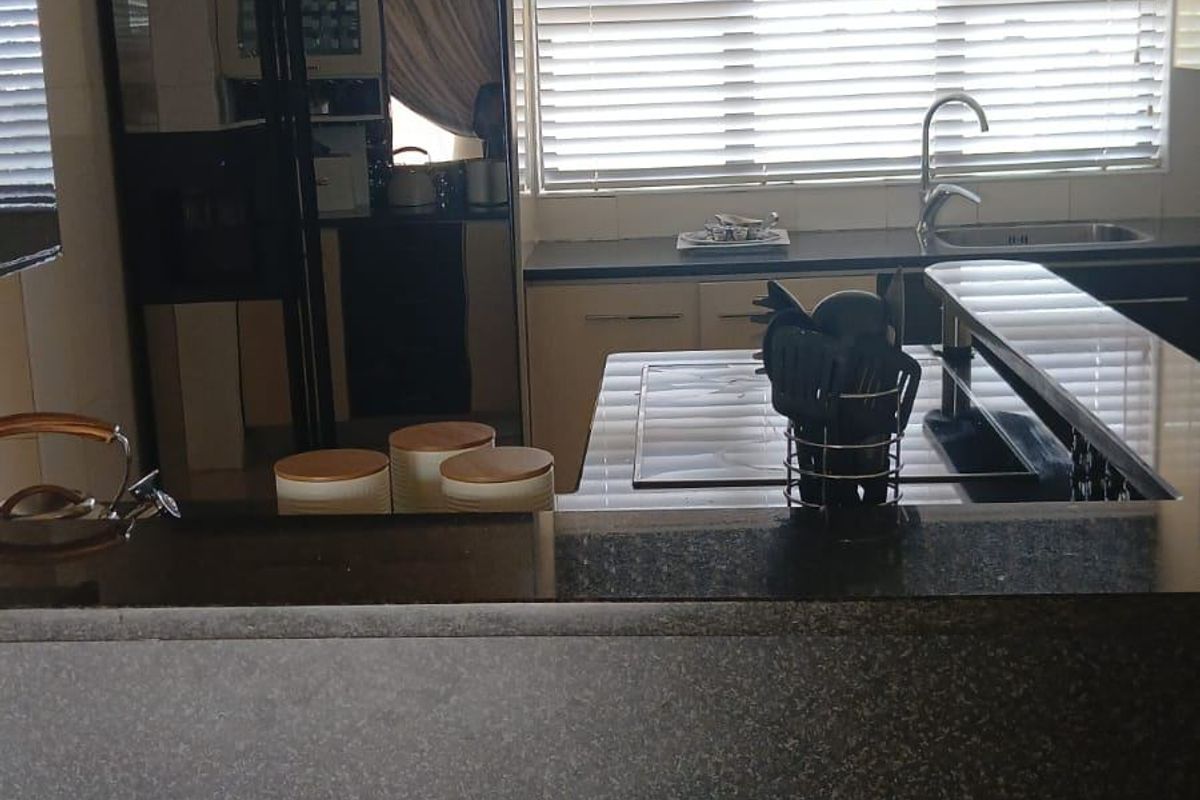 A functional kitchen featuring dark granite countertops, built-in cabinetry, a modern sink with mixer tap, and a built-in hob, illuminated by recessed lighting.