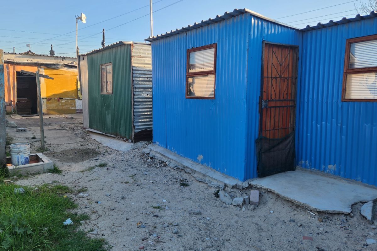 View of multiple corrugated metal structures on a residential plot, featuring basic security gates and concrete slab foundations.