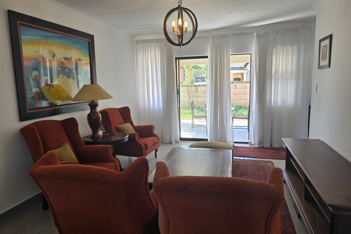 A comfortable living room featuring tiled flooring, a central pendant light, and a sliding glass door providing access to the rear patio area.