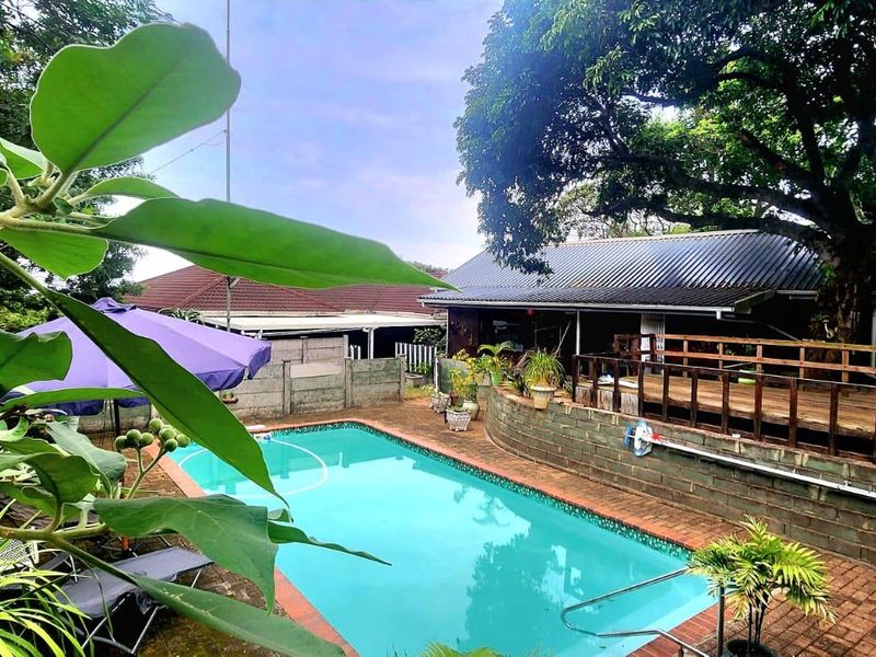 Outdoor pool area featuring a swimming pool, brick paved surround, and an elevated timber deck with railing, set within a landscaped garden.