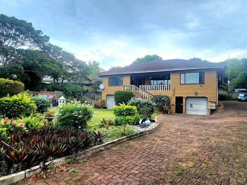 Front view of a brick house featuring a paved driveway, integrated garage, and an elevated balcony, set within a landscaped garden.