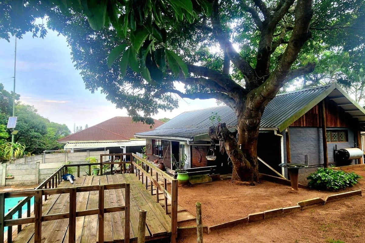 Rear exterior view featuring a wooden deck, swimming pool, and mature tree set within a garden area with boundary walling.