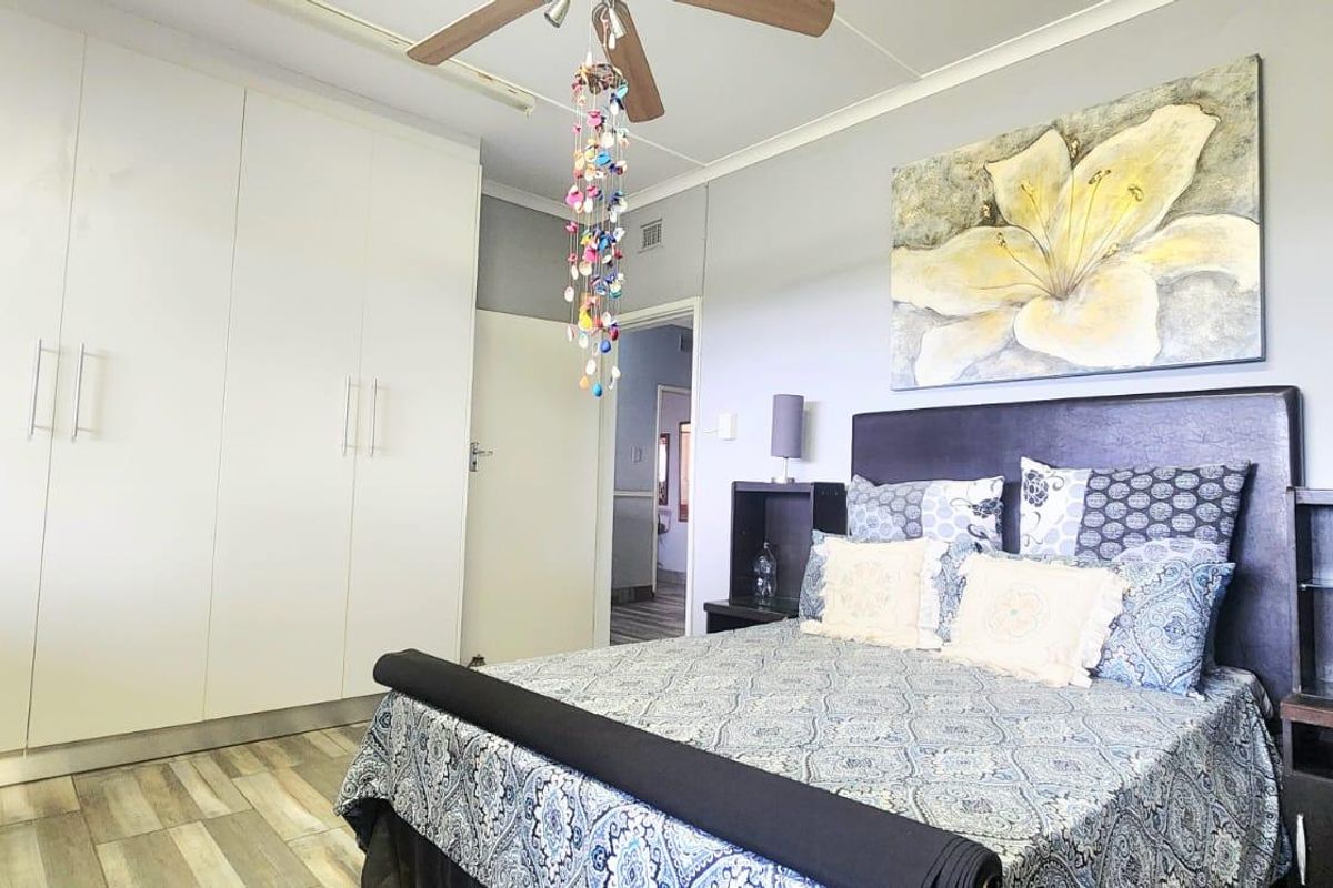A well-maintained bedroom featuring modern laminate flooring, ample built-in cupboard storage, and a ceiling fan.