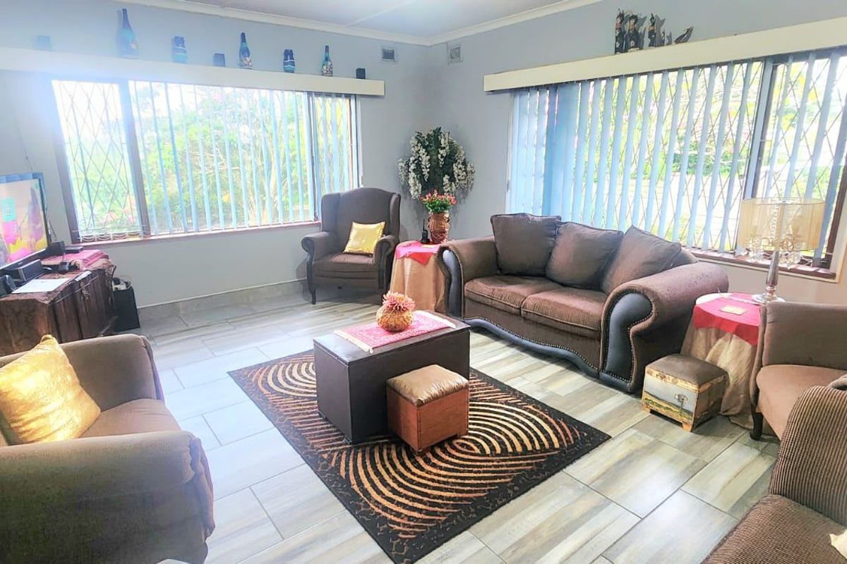 A spacious living room featuring tiled flooring, large windows with security bars, and vertical blinds, offering a bright and functional living space.