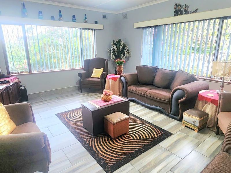 A spacious living room featuring tiled flooring, large windows with security bars, and vertical blinds, offering a bright and functional living space.