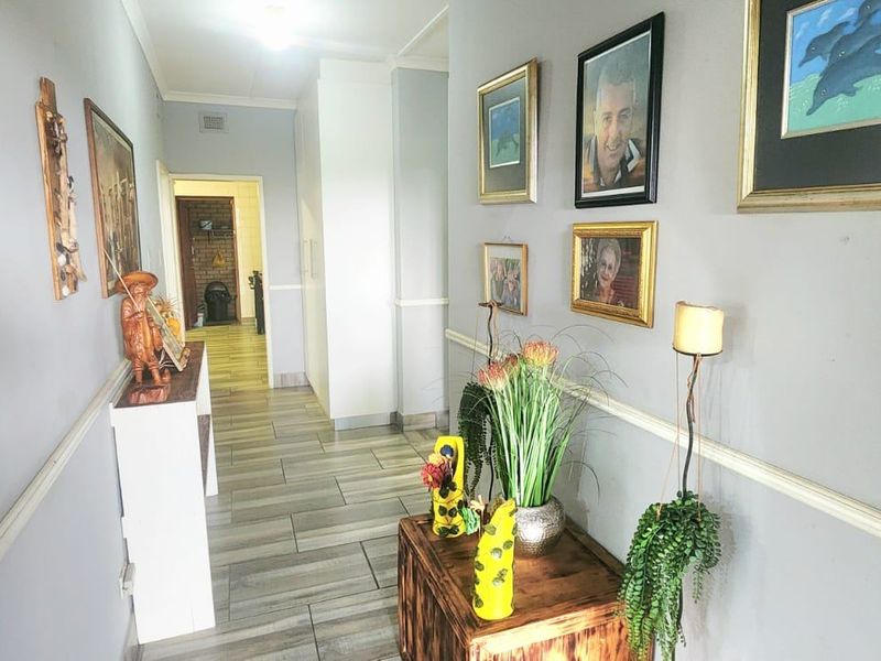 A well-lit interior hallway featuring neutral wall tones, decorative chair rail molding, and modern wood-look tiled flooring leading toward an adjacent room.