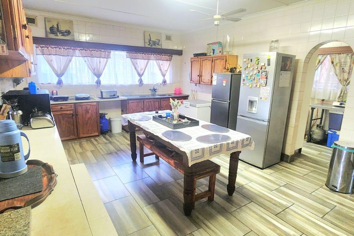 A functional kitchen featuring wooden cabinetry, tiled splashbacks, and tiled flooring, with an open archway leading to an adjacent utility area.