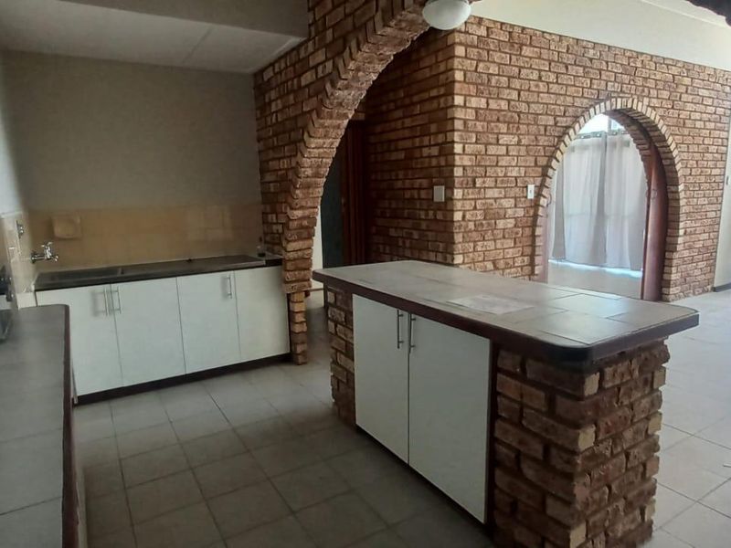 Open-plan kitchen and living area featuring distinctive brick archways, tiled flooring, and a central kitchen island with built-in cabinetry.