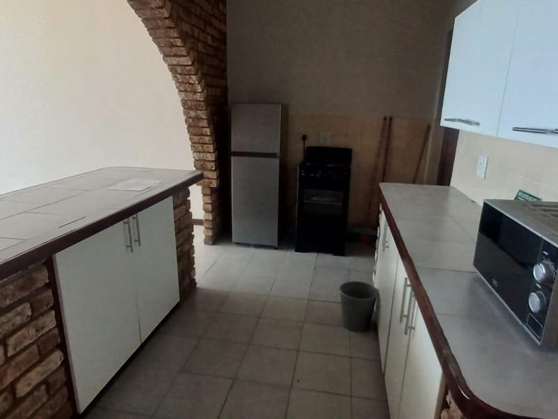 A functional kitchen featuring tiled countertops, built-in cabinetry, and a distinctive brick archway separating the space from the living area.