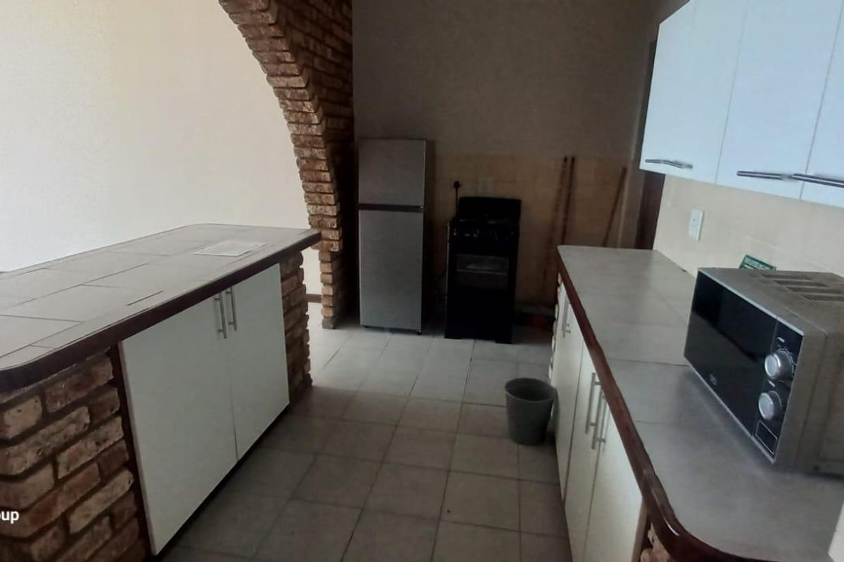 A functional kitchen featuring tiled countertops, built-in cabinetry, and a distinctive brick archway separating the space from the living area.