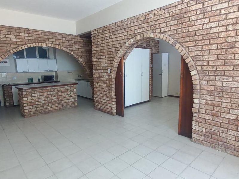 Spacious open-plan living area featuring distinctive brick archways, tiled flooring, and a functional kitchen with built-in cabinetry and a breakfast counter.
