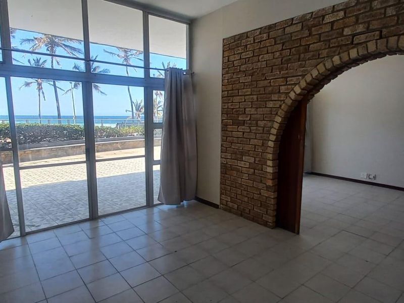 Spacious living area featuring an exposed brick archway, tiled flooring, and large floor-to-ceiling windows offering direct access to a patio with ocean views.