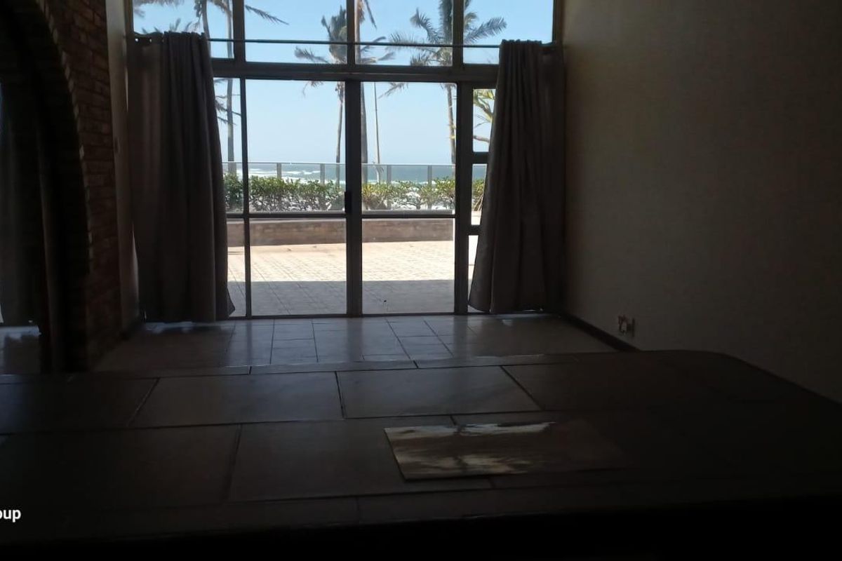 Spacious living area featuring large glass sliding doors that open to an outdoor patio with ocean views and an exposed brick archway.