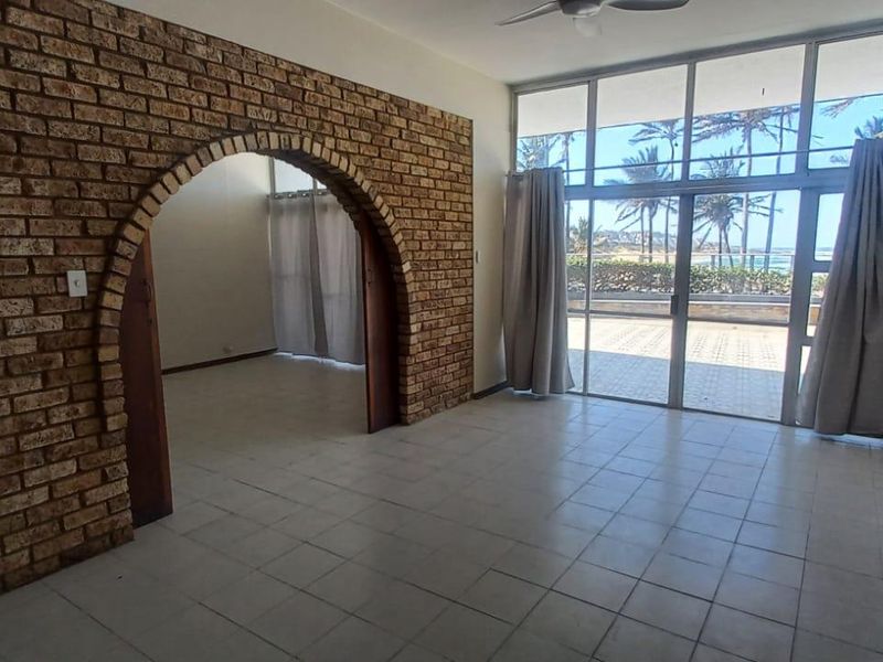 Spacious living area featuring a distinctive exposed brick archway, tiled flooring, and large sliding doors providing natural light and access to the outdoor area.