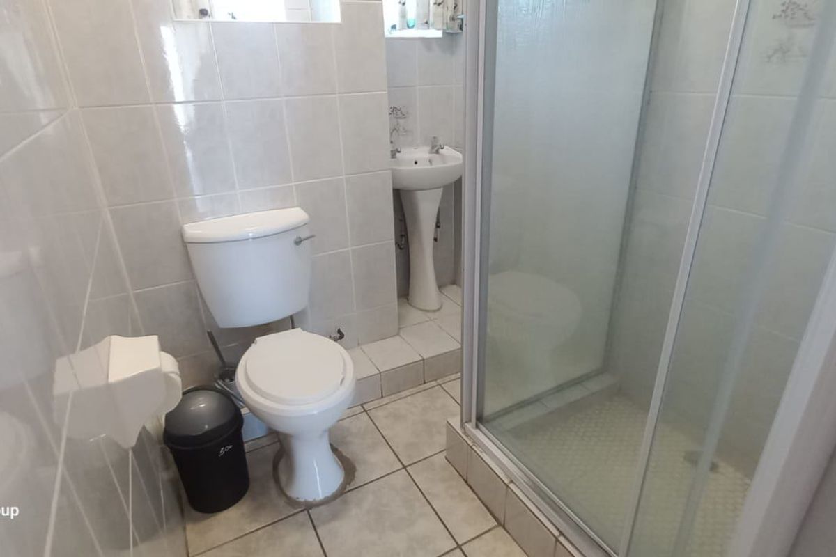 A functional bathroom featuring a shower enclosure, pedestal basin, and toilet with neutral wall and floor tiling.