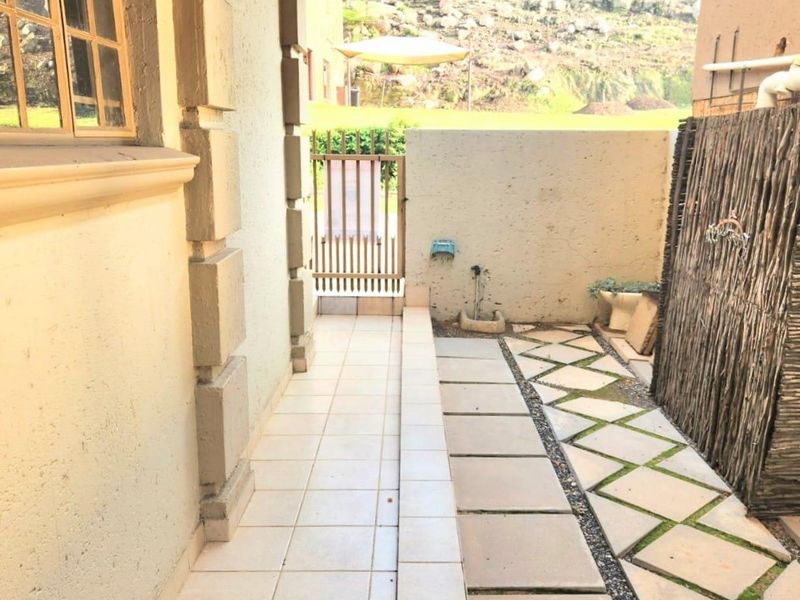 A side patio area featuring tiled flooring, a paved walkway, and a metal gate, providing access to the rear garden space.