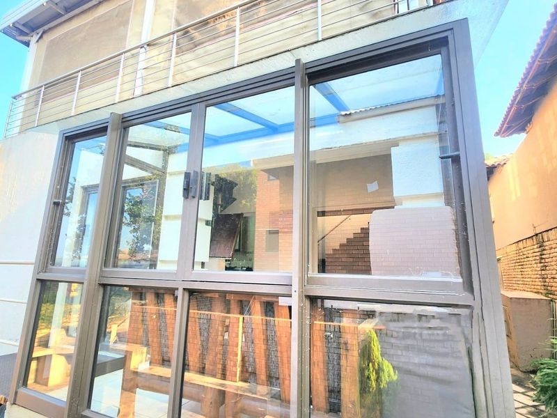 A modern glass-enclosed patio area featuring aluminium frames and tiled flooring, providing a bright and protected outdoor living space.