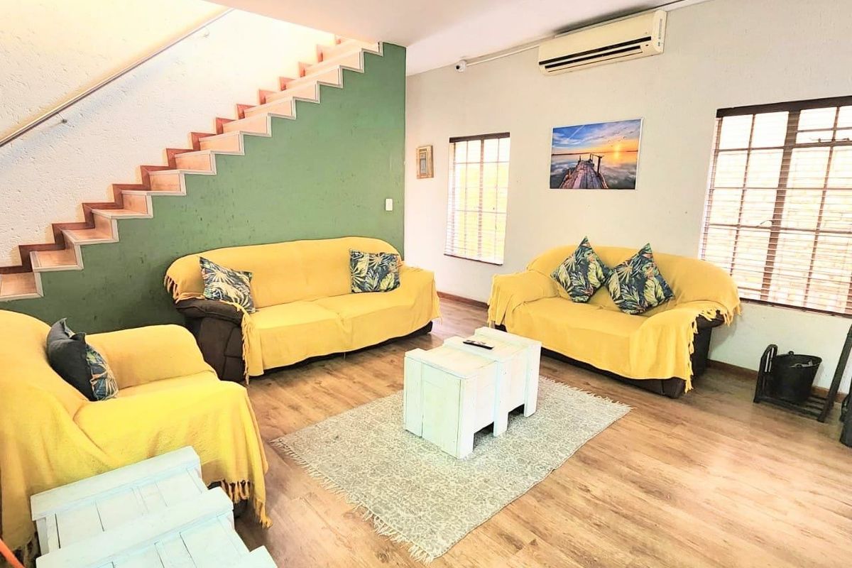 A spacious living room featuring laminate flooring, a staircase with a metal handrail, and a wall-mounted air conditioning unit.
