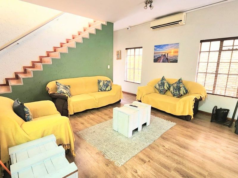 A spacious living room featuring laminate flooring, a staircase with a metal handrail, and a wall-mounted air conditioning unit.