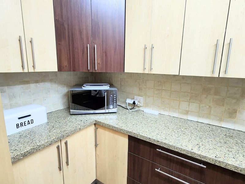 A functional kitchen corner featuring two-tone laminate cabinetry, granite countertops, and a neutral tiled backsplash.