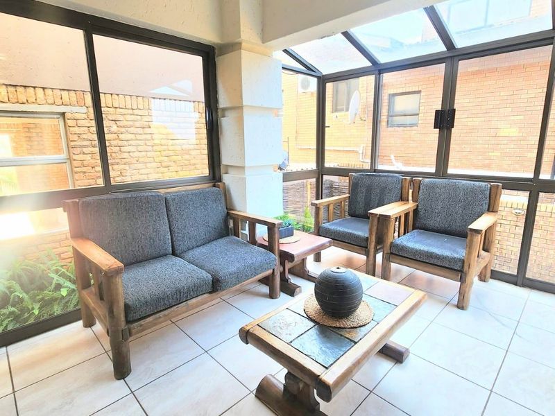 A bright, enclosed patio featuring tiled flooring, large glass windows, and a glass roof, providing a comfortable space for relaxation.