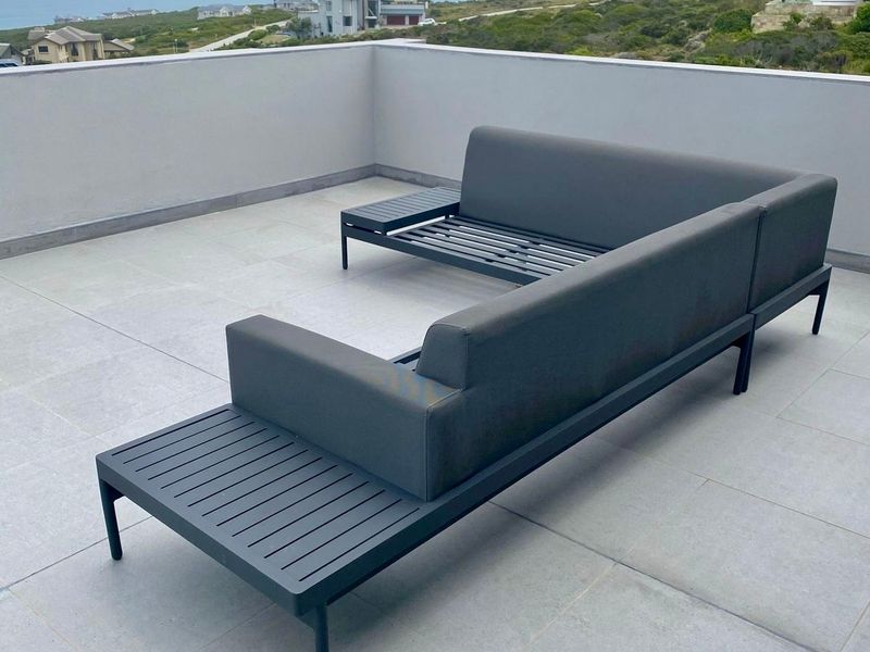 An open-air balcony featuring tiled flooring and a low parapet wall, offering expansive coastal and landscape views.